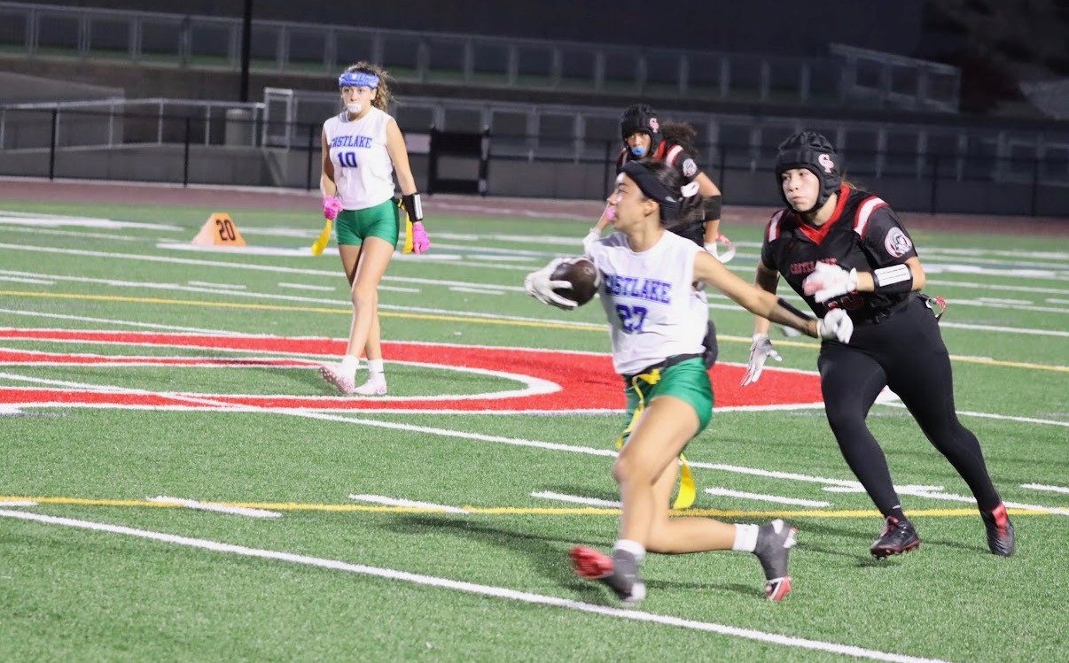 Kaylia Elsas, #27, carrying a football with a defender beside her on the field