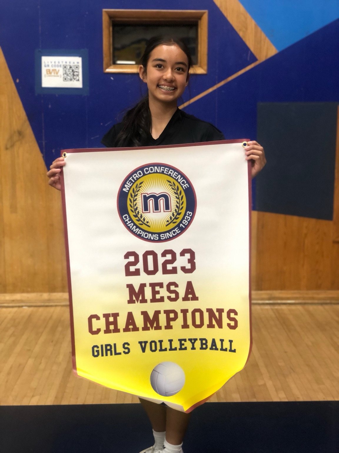 Kaylia holding a 2023 Mesa Champions girls volleyball banner